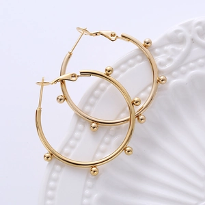 Detailed view of golden hoop earrings with bead accents on a white relief porcelain plate