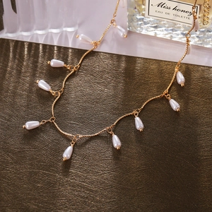 Detail of a gold heart pendant necklace with white teardrop pearls on a textured surface