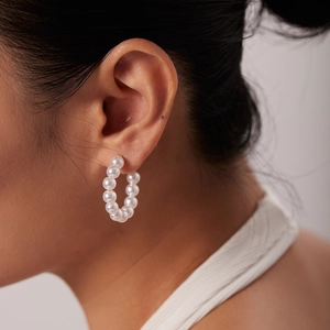 Detail view of large C-shaped hoop earrings made of white pearls on titanium steel