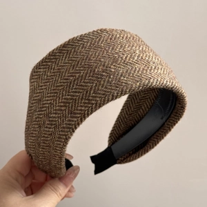 Detail of brown herringbone tweed headband with a wide-brim design and black inner lining