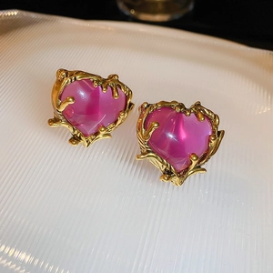 Close-up of heart-shaped gold earrings with purple gemstone on textured white base