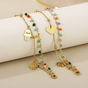 Detail of gold chain bracelets featuring colorful beads with heart and Hamsa hand charms