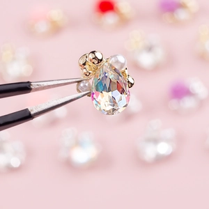 Teardrop crystal nail art charm with pearls and golden base on soft pink background