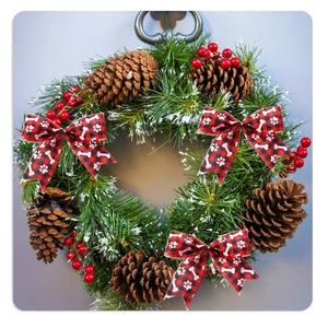 Christmas wreath with green needles, red berries, and dog paw print plaid ribbon bows