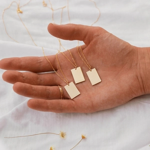 Detailed close-up of a minimalist gold layered necklace with rectangular pendant charms