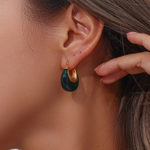Detail view of a gold U-shaped hoop earring with dark green resin inlay on a female model