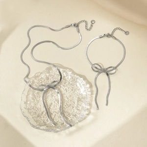 Detail of silver snake chain necklace and bracelet set with bow charms on beige fabric