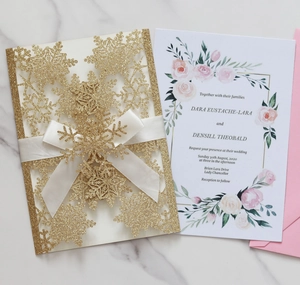 Detail of laser-cut gold snowflake wedding invitation with white ribbon and pink envelope
