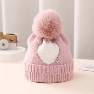 Detail of pink knitted baby hat with white heart pattern and fluffy pompom