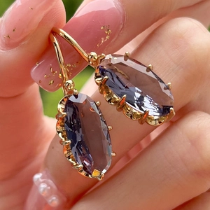 Macro shot of gold-plated drop earrings with oval faceted purple gemstone settings