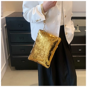 Detail shot of a mini golden sequin clutch bag with leather handle held by a model
