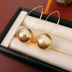 Détail de boucles d'oreilles boules dorées brossées avec crochet sur un présentoir à bijoux