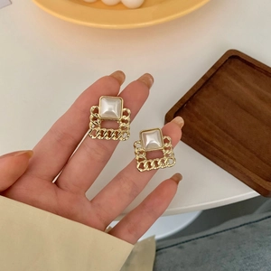 Detailed macro view of square gold chain earrings with inlaid white pearls on hand