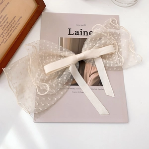 Detail of a beige lace bow hair clip with polka dots and silk ribbon on a light desk