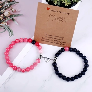 Detail of magnetic stone bracelets for couples with Pinky Promise card on marble background