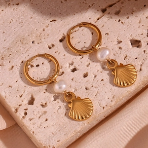 Macro view of gold plated hoop earrings featuring white freshwater pearl and shell charms