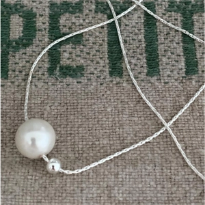 Close-up of minimalist single white pearl pendant on fine silver chain over linen fabric