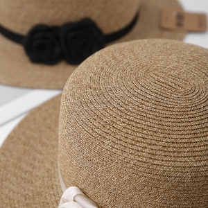 Detail of woven straw hat texture featuring black rose accents and silk ribbon bows
