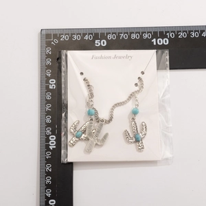 Detailed view of silver cactus earrings with blue beads on white card with scale ruler