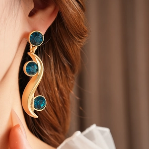 Close-up of vintage gold S-shaped wave earring with three blue sapphires on a model