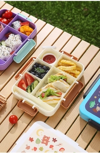 Outdoor picnic scene showing various colorful multi-compartment bento boxes on a wooden table