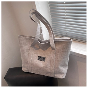 Detail of grey woven fabric tote bag with black fashion label and dual handles