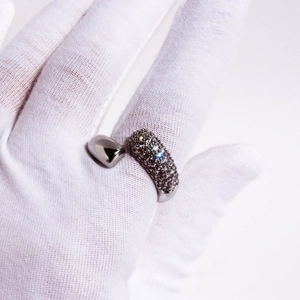 Close-up of open ring with dense dark gemstones held by a hand in a white glove