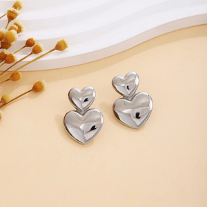 Detailed shot of polished silver double heart stud earrings on a warm beige background