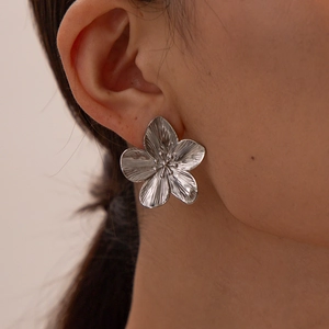 Macro detail of silver flower earrings with brushed metal texture worn by a model