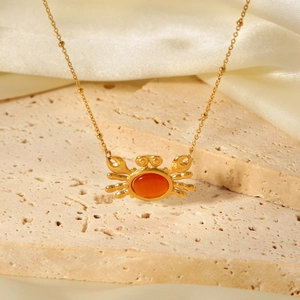 Macro view of gold crab pendant with orange stone and bead chain on stone base
