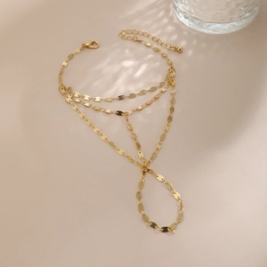 Detail of gold layered hand chain with round disc link design and ring on beige surface