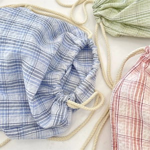 Detail of plaid canvas drawstring backpacks in blue, green, and red with thick cotton ropes