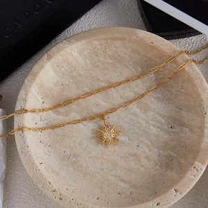 Dettaglio della collana con pendente a sole dorato e strass su vassoio in pietra