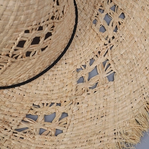 Detail of hollow woven raffia straw hat with fringe edges and black decorative cord