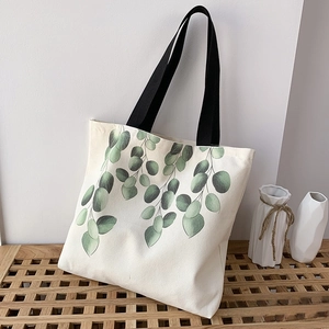 Detail of canvas tote bag with green eucalyptus leaf print and black woven handles