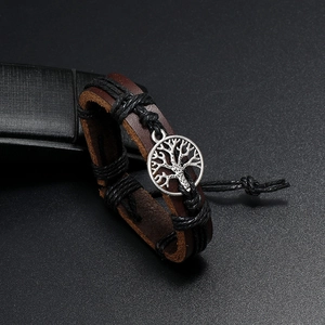 Detailed close-up of woven brown leather bracelet with silver tree of life charm