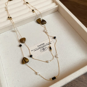 Detail of vintage double-layer necklace with golden chains and heart-shaped tiger eye beads