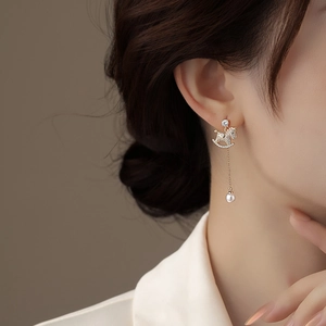 Detail of gold rocking horse earring with pavé zircon stones and a hanging white pearl
