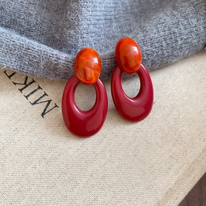 Macro shot of retro acrylic oval earrings with orange marble finish and red hollow pendant