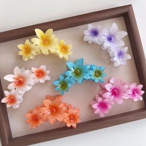 Detailed view of large flower hair claws in six candy colors arranged on a beige tray