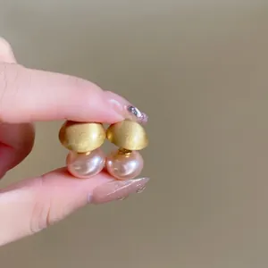 Detail of matte gold studs with pink pearls held against a warm beige background