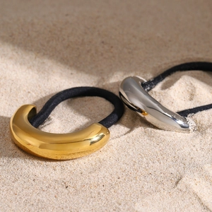 Detail view of minimalist gold and silver metal hair ties on a sandy beach setting