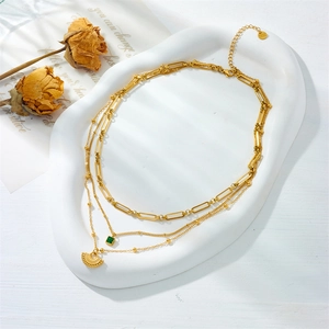 Detail of layered gold stainless steel necklace with green square gem and fan pendant