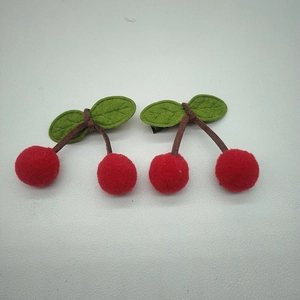 Close-up of cute handmade cherry hair clips with plush red pom-poms and green felt leaves