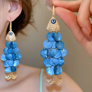 Detail of fish-shaped earrings with blue shell scales and golden metal hooks for beach style