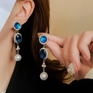 Dettaglio di orecchini di lusso con cristalli blu e perla bianca su un modello elegante