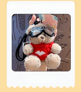 Close-up of a plush brown bear keychain wearing a red heart sweater and goggles