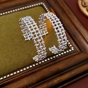 Detailed macro view of silver hoop earrings with a textured woven mesh design on velvet