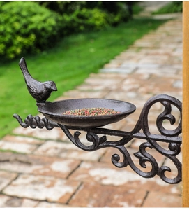 Macro detail of cast iron bird feeder tray filled with seeds on garden wood post