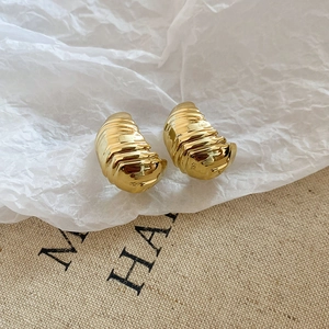 Macro shot of gold croissant earrings with spiral texture on rustic fabric background
